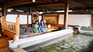 Una tradizionale onsen giapponese con vasca in pietra, panche in legno e pavimento in tatami.