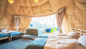 Un'accogliente sistemazione in tenda con due letti, una poltrona e un'area pranzo.