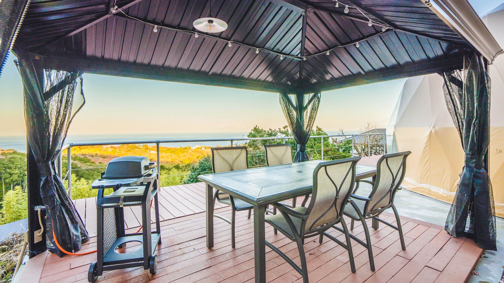 Um pátio externo com mesa e cadeiras, churrasqueira e vista para o oceano.