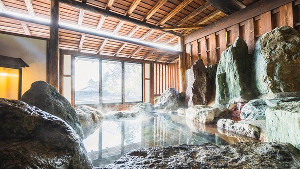 Un’onsen tradizionale giapponese con travi in legno, grandi rocce e una vasca termale.