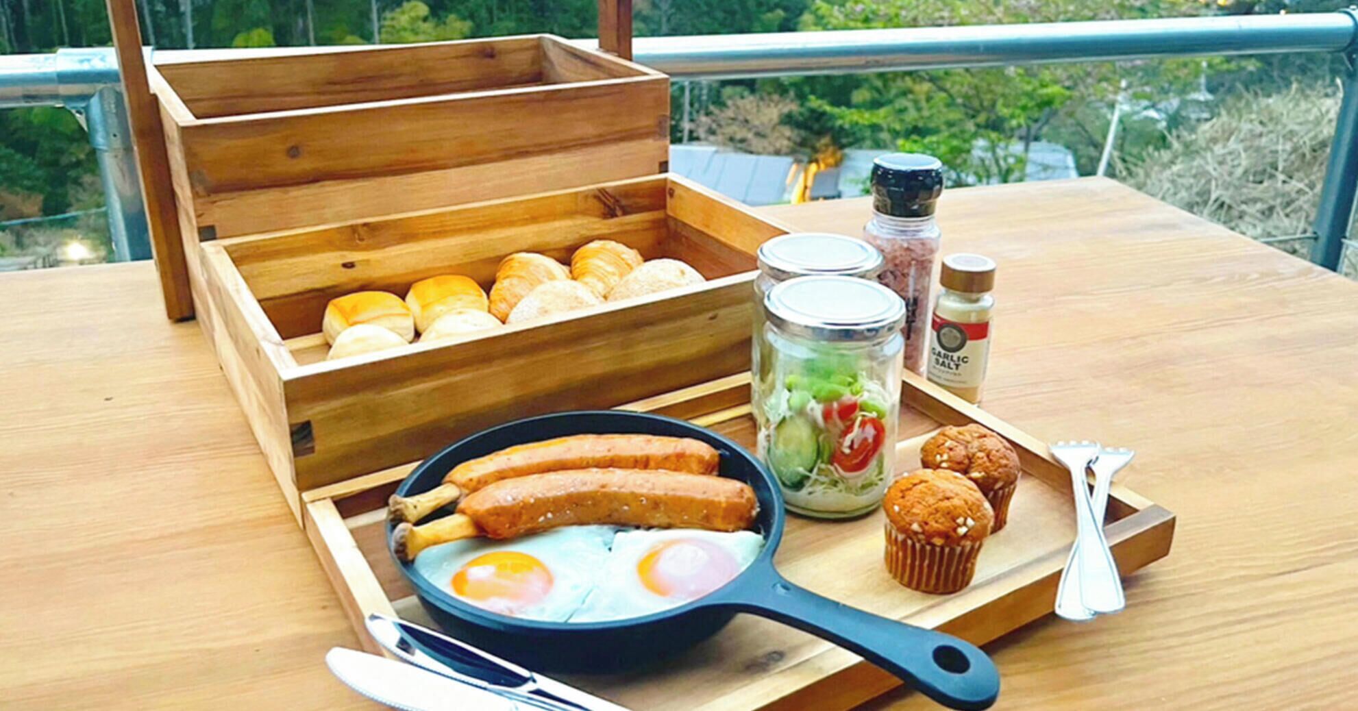 A wooden table with a tray containing sausages, eggs, muffins, and a jar of pickles.