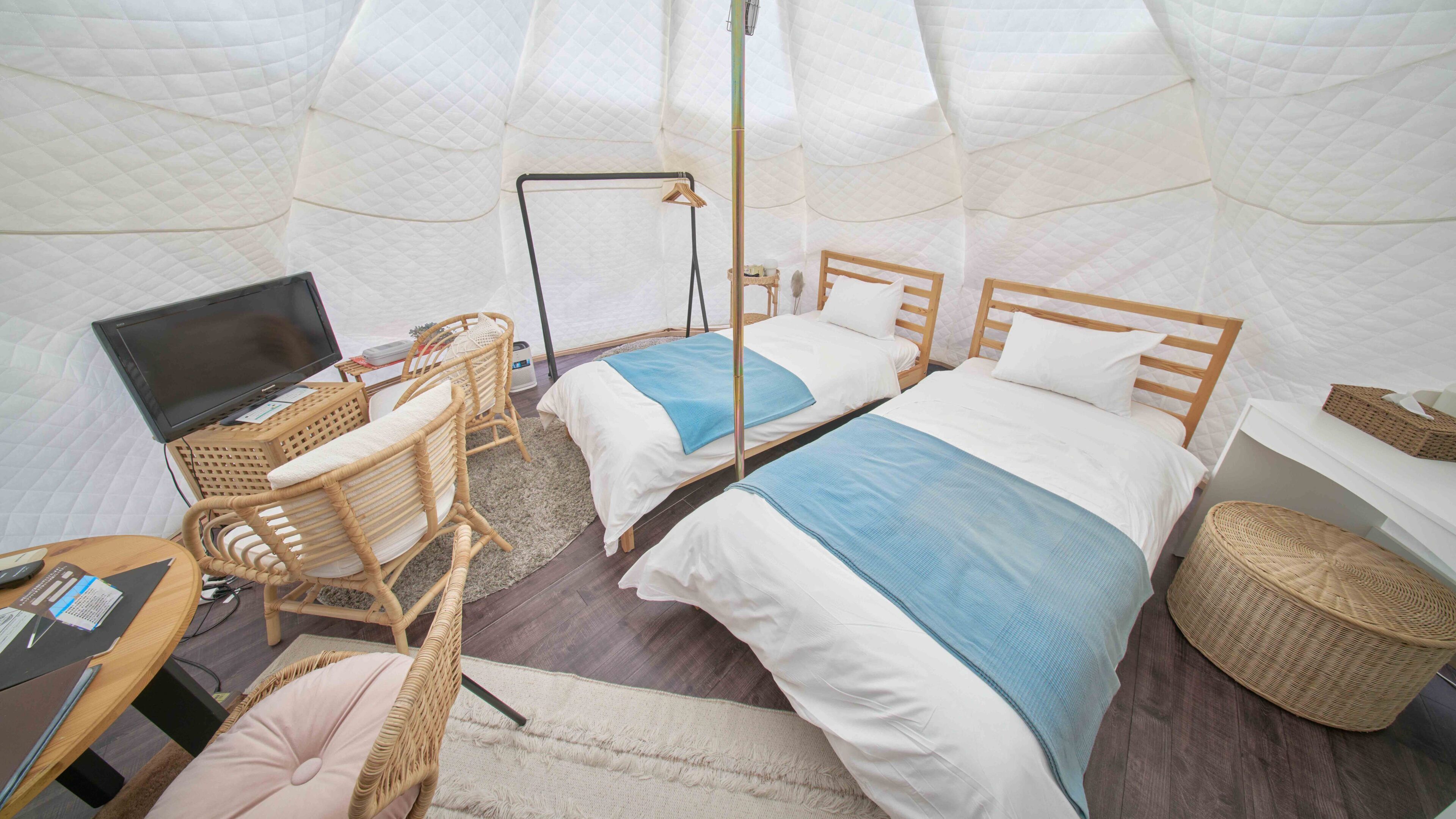 Een tent-achtige kamer met twee bedden, een bureau met een laptop, rieten stoelen en een bedlampje.