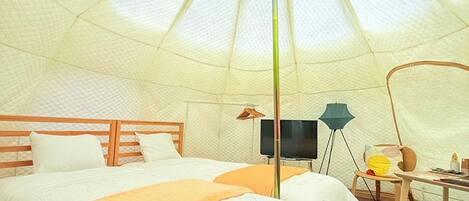 A tent-style room with two beds, a television, and a desk.