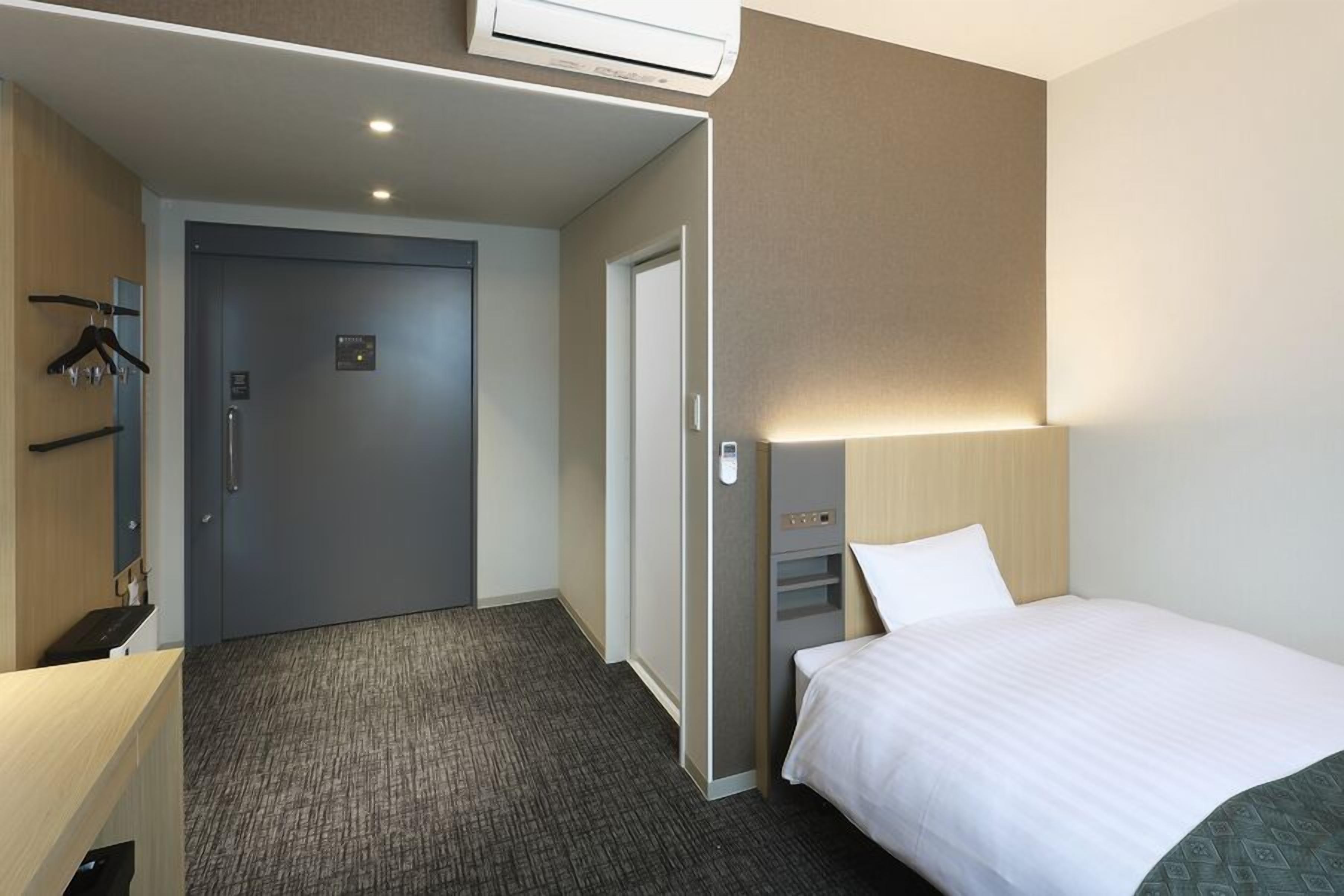 Une chambre d’hôtel avec un lit, un bureau, une chaise, une armoire et une porte.