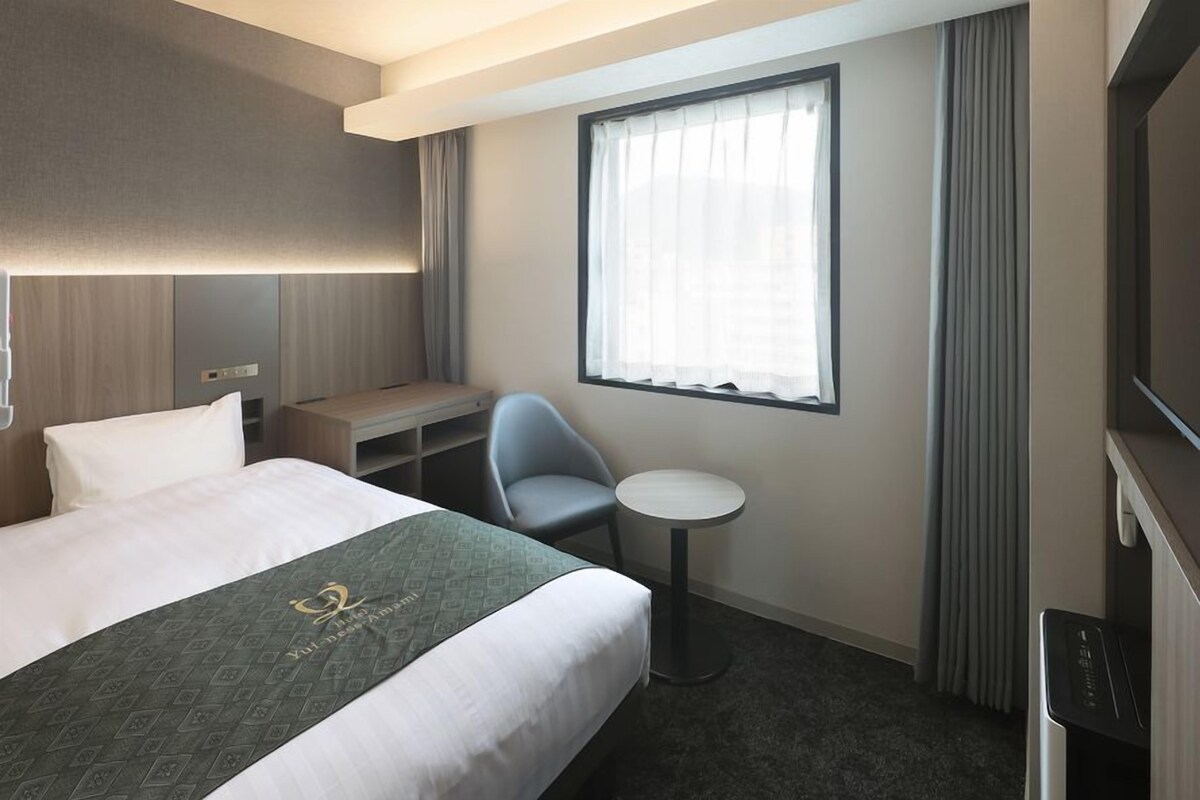 Habitación de hotel con cama, escritorio, silla, mesita y televisor.