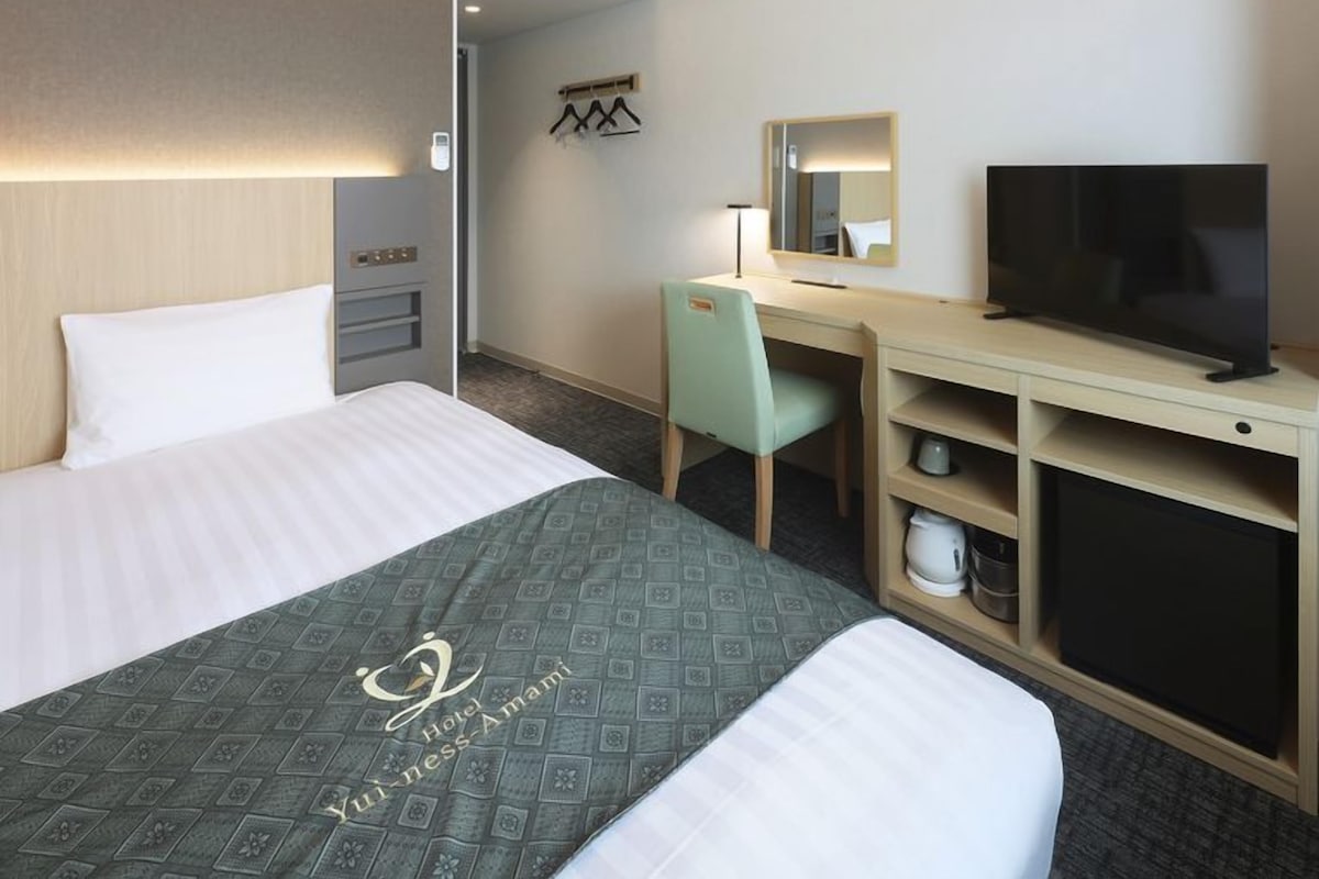 A hotel room with a bed, a desk with a chair, a television, and an air conditioning unit.