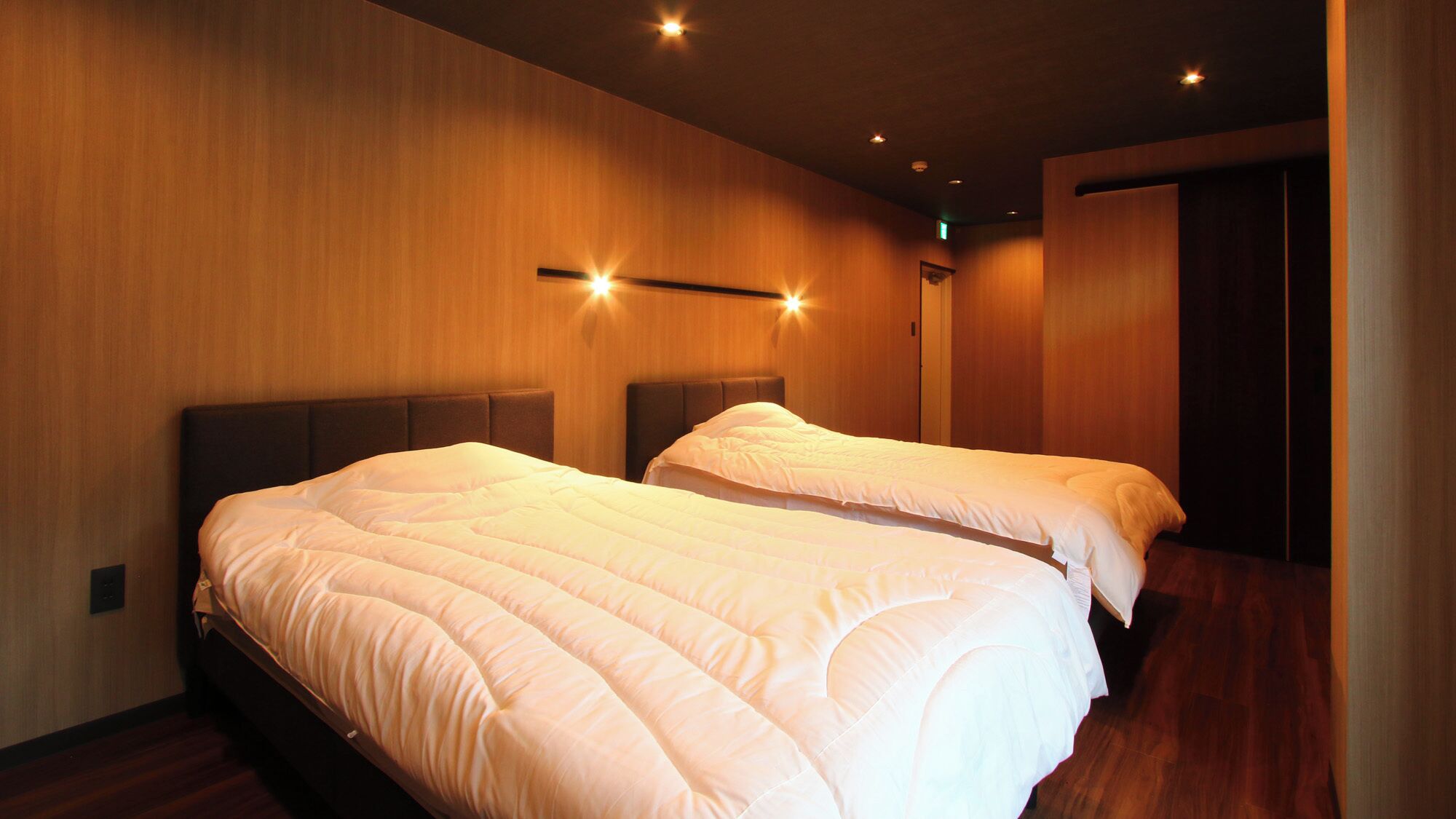 A hotel room with two beds, wooden walls, and recessed ceiling lighting.