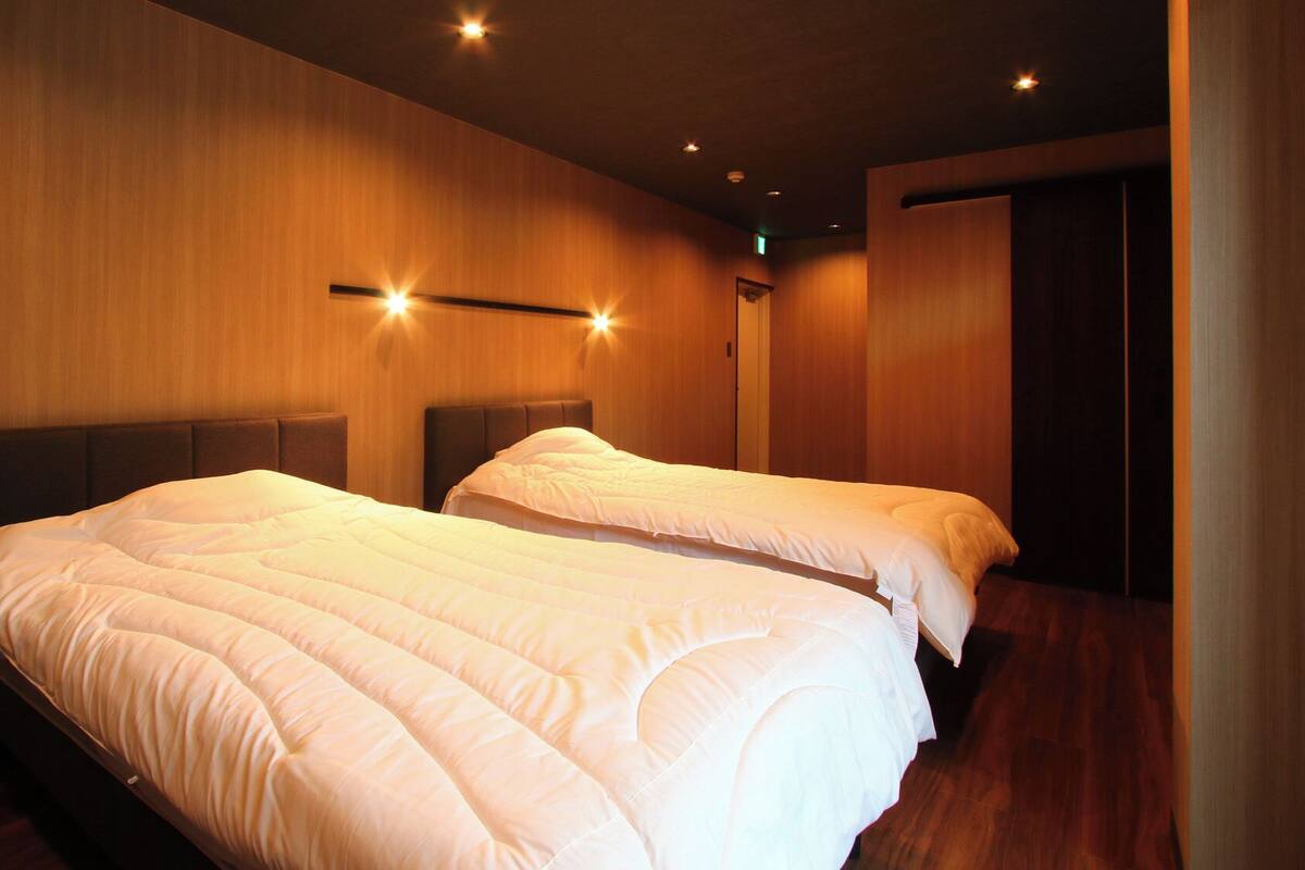 A hotel room with two beds, wooden walls, and recessed ceiling lighting.