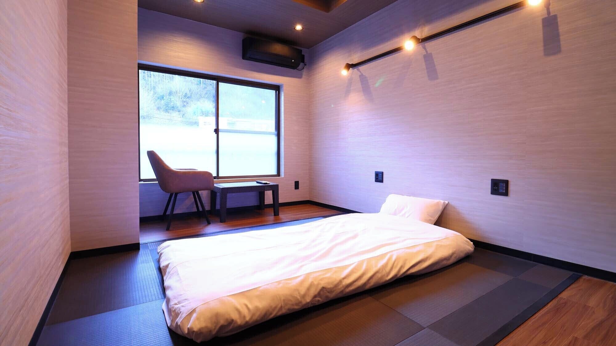 A modern hotel room with a bed, a chair, a small table, and a large window.