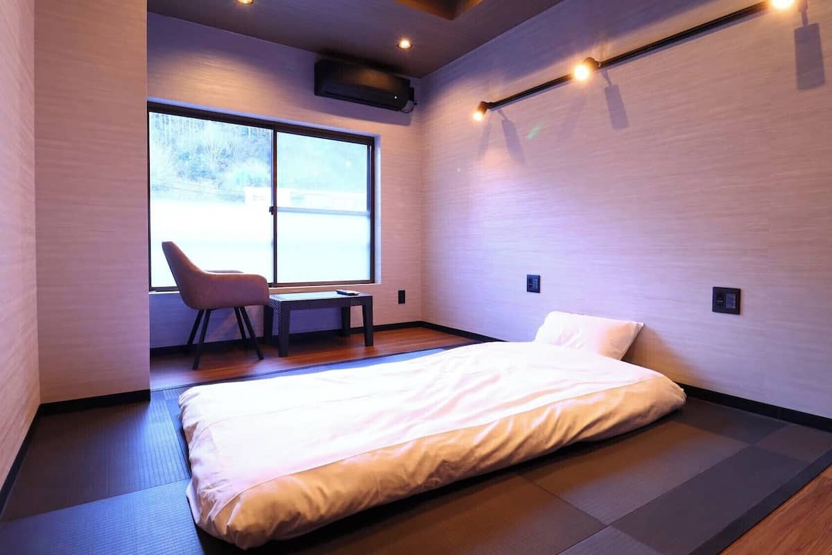 A modern hotel room with a bed, a chair, a small table, and a large window.