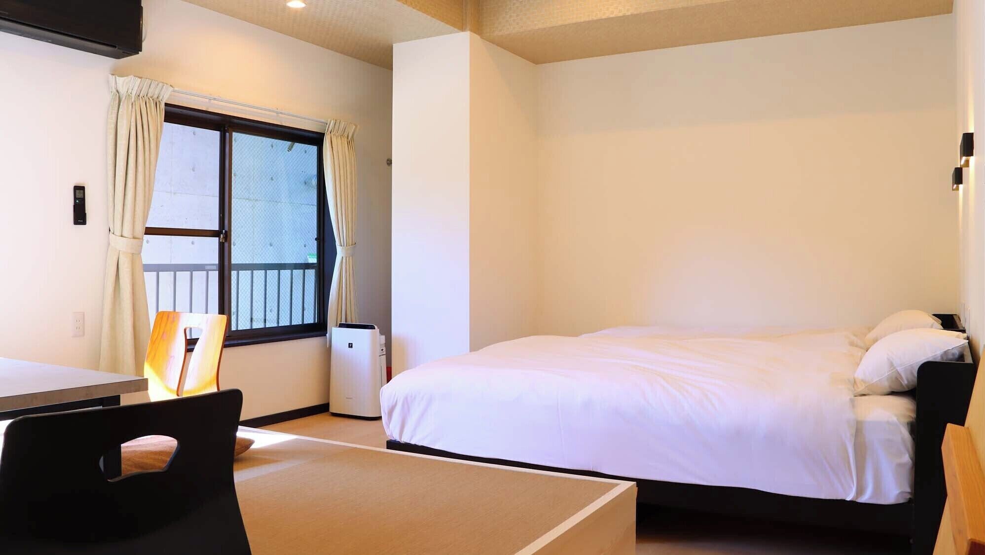 A hotel room with a bed, a desk, a chair, and a window with curtains.