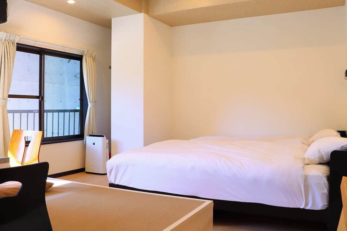 A hotel room with a bed, a desk, a chair, and a window with curtains.