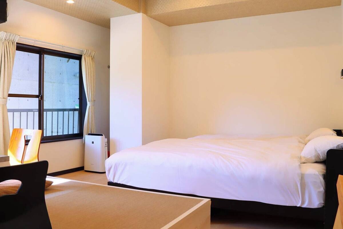 A hotel room with a bed, a desk, a chair, and a window with curtains.