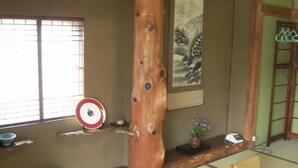 A traditional Japanese room with tatami flooring, a shoji screen, a wooden pillar, a shelf with a decorative plate, a vase, and a bed with a futon. - Tamayama Onsen Tamaya Ryokan (Iwaki)
