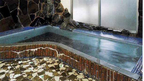A spa area with a stone wall, a tiled floor, and a glass door leading outside. - Tamayama Onsen Tamaya Ryokan (Iwaki)