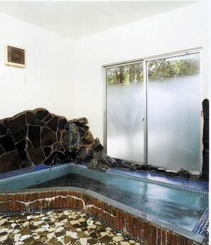 A spa area with a stone wall, a tiled floor, and a glass door leading outside. - Tamayama Onsen Tamaya Ryokan (Iwaki)