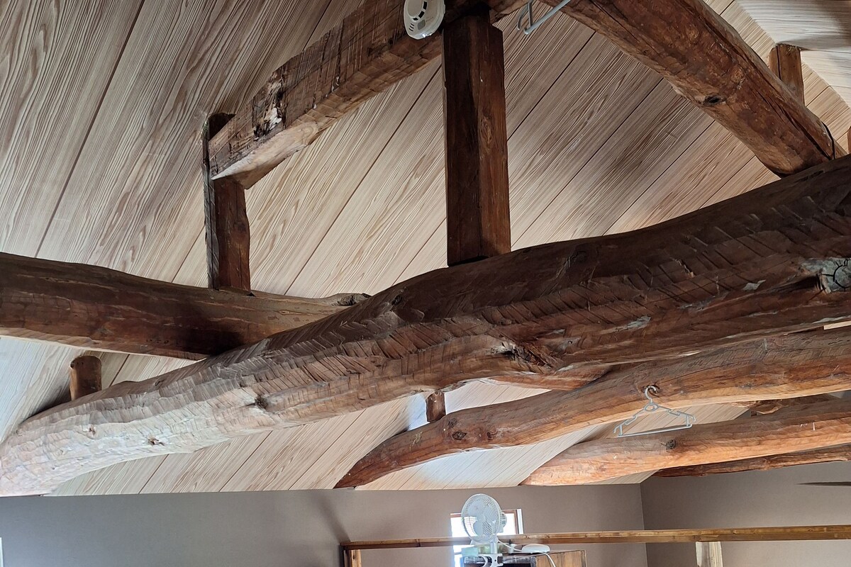 A rustic bedroom with exposed wooden beams, a bed with white bedding, and a fan on a wooden nightstand.