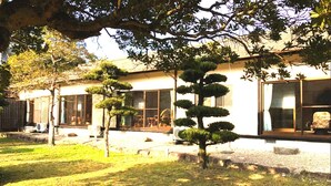 A building with a traditional architectural style, featuring large windows and a well-maintained garden with several bonsai trees. - Kumanokawa Onsen Minshuku Mimi (Saga)