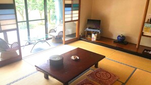 A traditional Japanese room with tatami flooring, a tatami mat in the center, a low table with a tea set, a television on a stand, and a sliding door leading to a balcony. - Kumanokawa Onsen Minshuku Mimi (Saga)