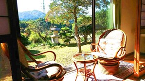 A room with a view of a garden and mountains. There are two chairs and a small table. - Kumanokawa Onsen Minshuku Mimi (Saga)