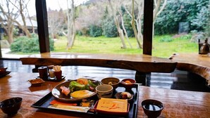 A dining table with a variety of dishes, including sushi, sashimi, and a bowl of soup, set against a backdrop of a wooden bench and a view of a garden. - Hananoki Inn (Sado)