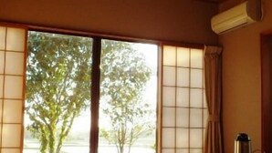 A traditional Japanese-style room with tatami flooring, a low wooden table, and a view of trees through shoji screens. - Hananoki Inn (Sado)