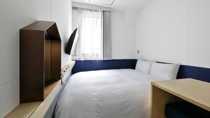 Habitación de hotel con una cama, una mesita de noche de madera, un televisor de pantalla plana en la pared y una ventana con cortinas.