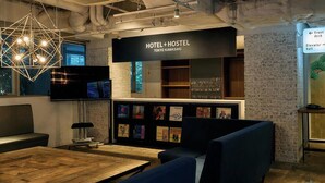 Interior moderno de hotel y albergue, con una recepción, zona de estar y una pared decorada con diversos objetos.