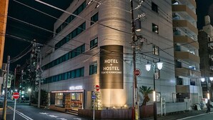 Un moderno edificio de hotel y albergue con fachada curva, varios pisos y una entrada destacada con un letrero que dice "HOTEL + HOSTEL TOKYO KAWASAKI".
