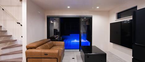 A modern living room with a sofa, a flat-screen TV, and a staircase.