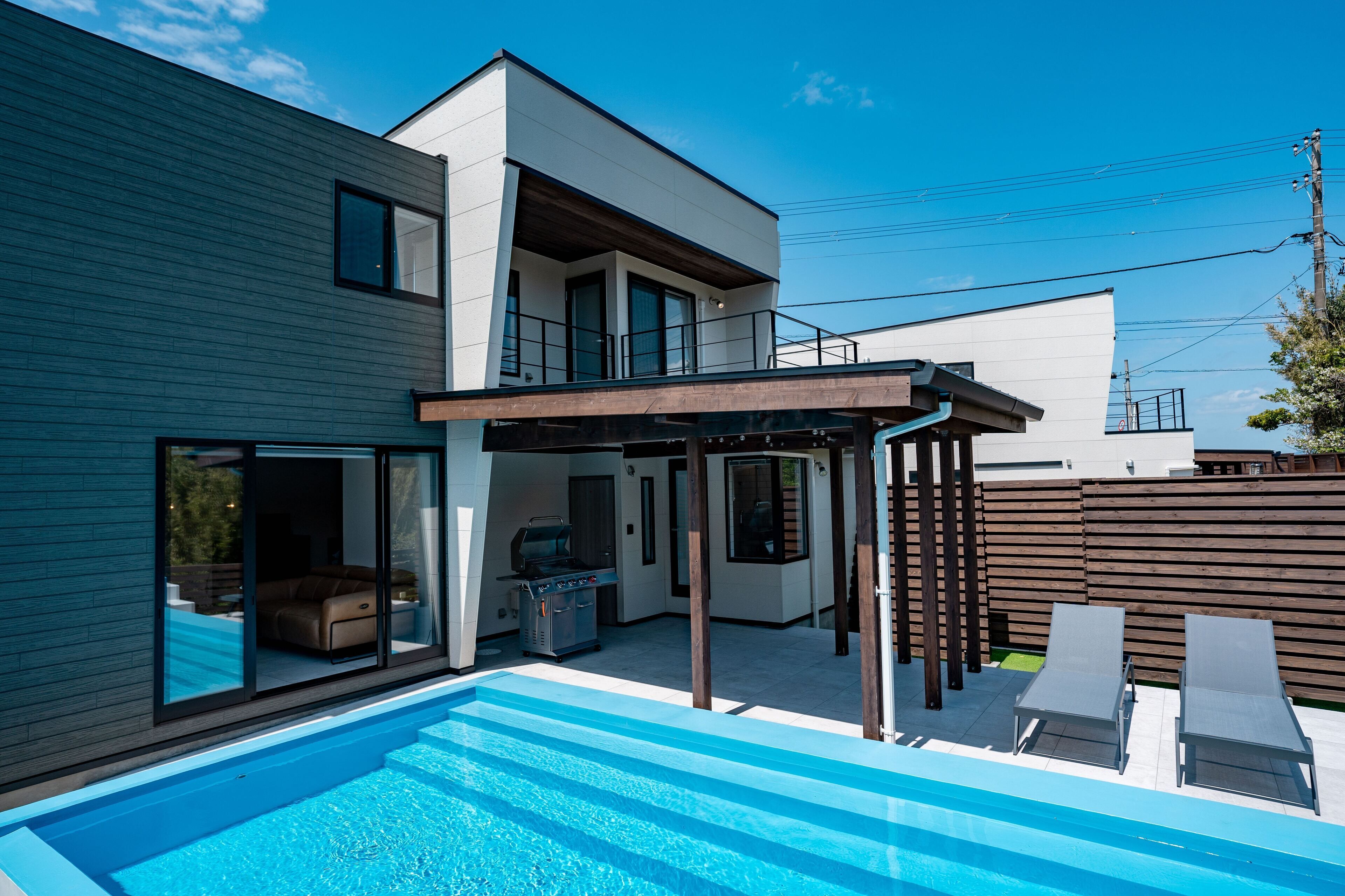 A modern two-story house with a swimming pool, outdoor seating, and a barbecue area.
