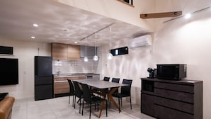 Een moderne keuken met een eethoek, met een grote tafel, zwarte stoelen en een donkere kast.