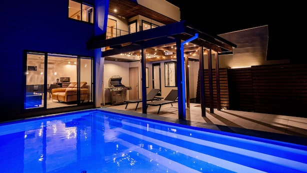 Een modern huis met een zwembad, een overdekt terras en een barbecueplek.