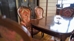 Una habitación tradicional japonesa con suelo de tatami, una mesa de madera baja y sillas con intrincados diseños rojos y dorados.