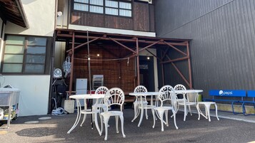 Un área de estar al aire libre con sillas y mesas de metal blanco, la entrada de un edificio de madera y un letrero de Pepsi.