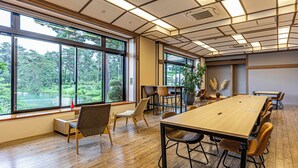 Un salón de conferencias con una gran mesa, varias sillas y ventanas amplias que dan a una zona boscosa.