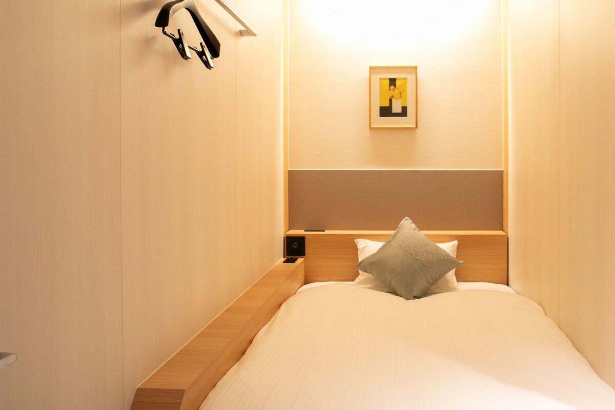 Un dormitorio pequeño y ordenado con una cama individual, una mesita de noche y un estante en la pared.