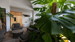 A modern indoor patio with wicker furniture, a bathtub, and lush green plants. - 730 Hotels (Ishigaki)