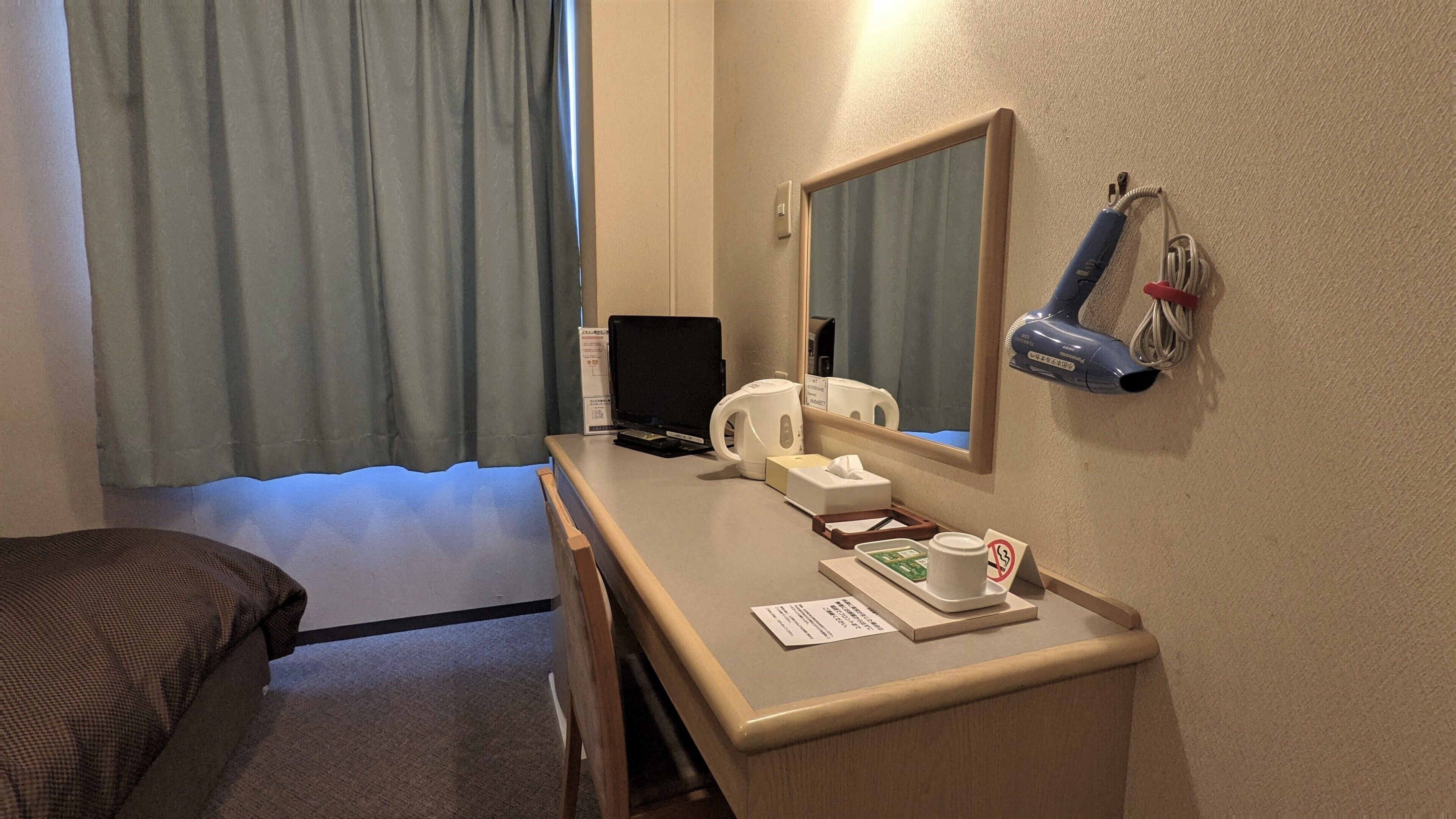 A hotel room with a bed, a desk with a laptop, a kettle, a mirror, and a hairdryer.