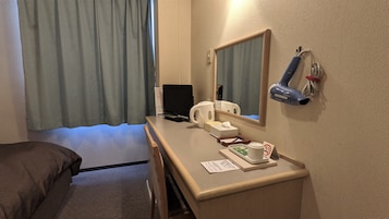 Habitación de hotel con cama, escritorio con una laptop, hervidor de agua, espejo y secador de pelo.