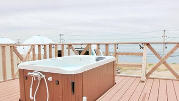A wooden deck with a hot tub, overlooking a body of water.