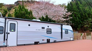 A white RV with the brand name 'AVENGER' on the side, parked on a paved area with a wooden fence and trees in the background. - Costa Blu Awaji Island West Coast (Awaji)