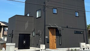 Un edificio moderno de dos pisos con fachada oscura, puerta de madera y una ventana pequeña.