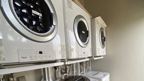 A row of three front-loading washing machines and two stacked top-loading machines in a laundry room. - Chi Chi Nu Ji (Kunigami)