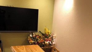 A dining area with a wooden table and chairs, a flat-screen TV mounted on the wall, and a wall-mounted light fixture. - Chi Chi Nu Ji (Kunigami)