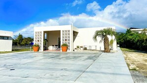 A modern building with a covered outdoor seating area, potted plants, and a palm tree. - Chi Chi Nu Ji (Kunigami)