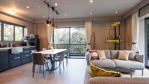 Un salon moderne avec un canapé, une table à manger et des chaises. Il y a un balcon avec vue sur les arbres.