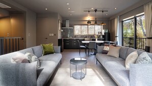 Un salon moderne avec un canapé gris, une table basse ronde et une cuisine en arrière-plan.