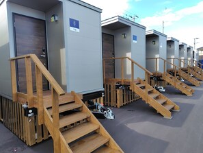 A row of portable cabins with wooden staircases leading to the entrance. Each cabin has a door and a small sign above it.