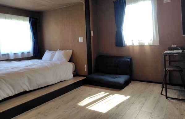 A room with a bed, a small seating area, a desk, and a window with curtains.